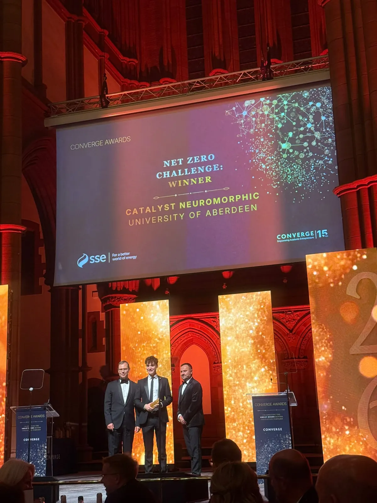 The Net Zero Challenge winner slide on the screen at Barony Hall, with Catalyst Neuromorphic on stage below